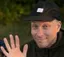 Aleksi facepicture wearing a black cap and waving his right hand.
